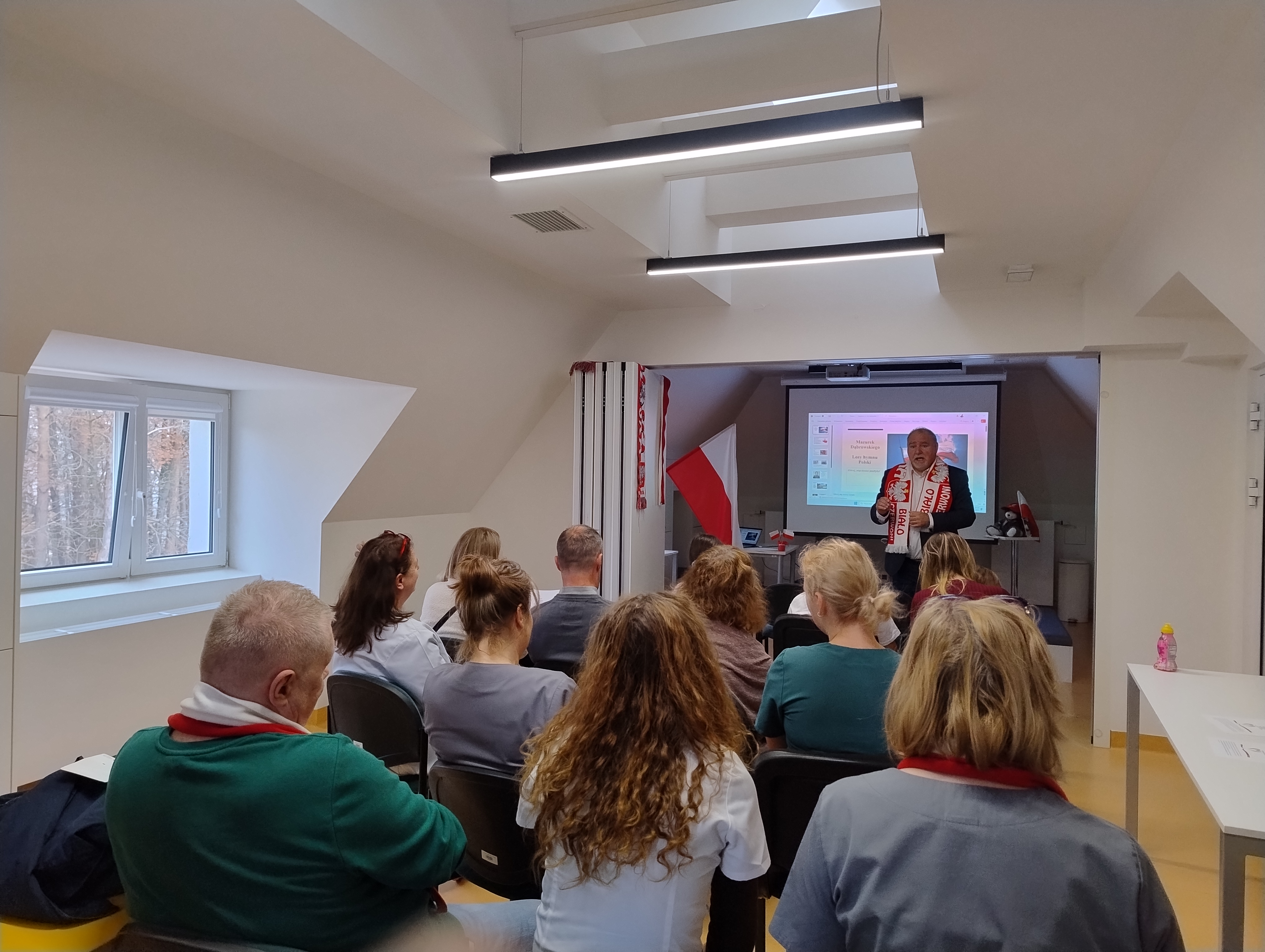 stojący mężczyzna i siędzący na krzesełkach ludzie img_20251107_111036373_hdr.jpg